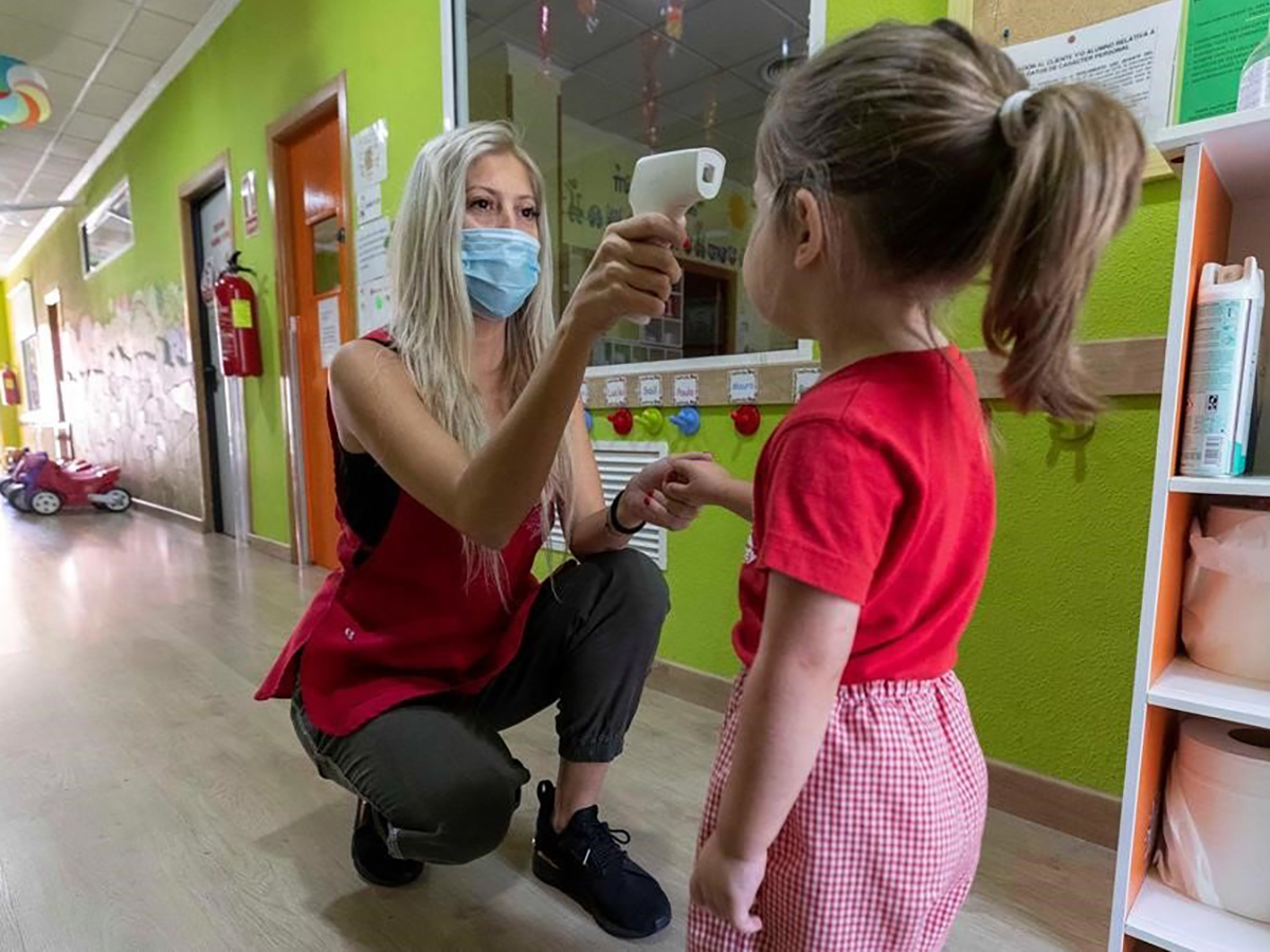 Mujer toma la temperatura de una niña en una escuela infantil en plena crisis del COVID 19